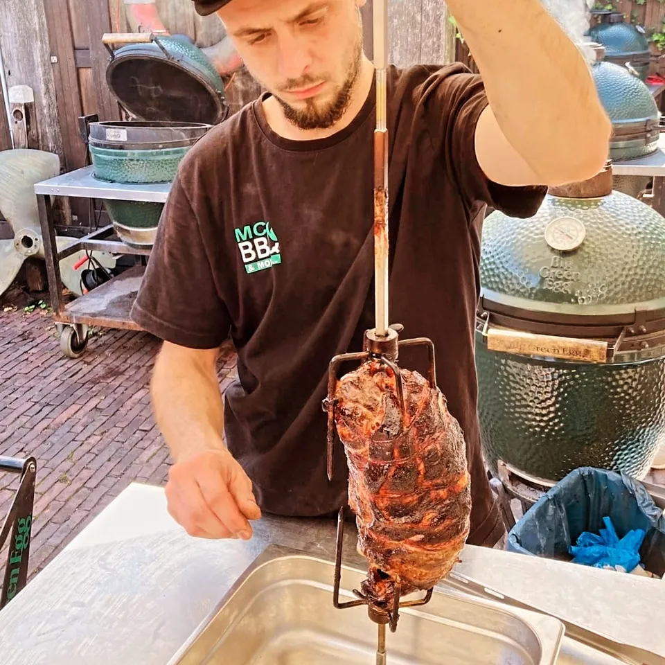 Mitch werkt met een stuk bereid vlees aan het spit naast de barbecues